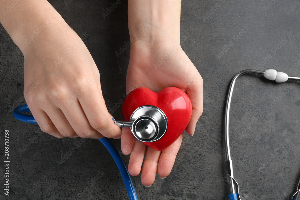 Female hands with stethoscope and small heart on dark grey background