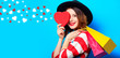 © Masson - smiling red-haired white european woman in hat and red striped shirt with heart shape toy and shopping bags on blue background with hearts