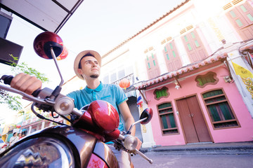 Wall Mural - Enjoying trip. Young smiling man  driving scooter on asian street.