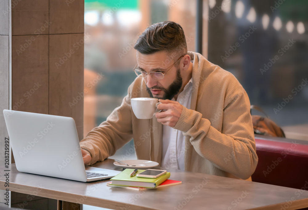 Young freelancer with cup of coffee and laptop working in cafe