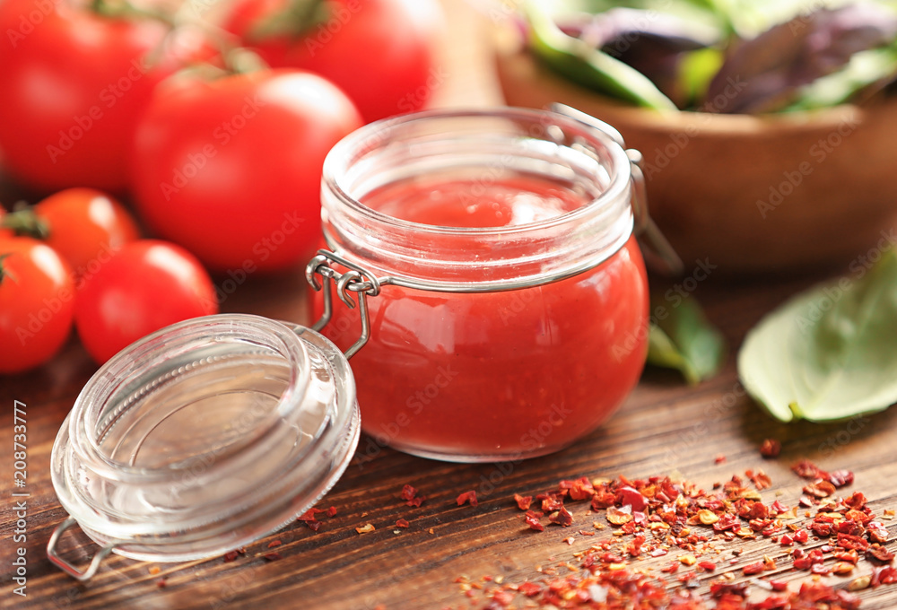 Delicious red sauce in glass jar and ingredients on table