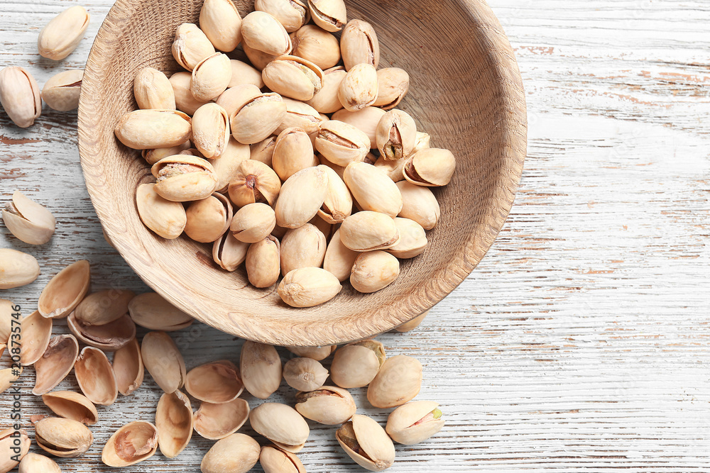 Bowl with pistachio nuts on wooden background