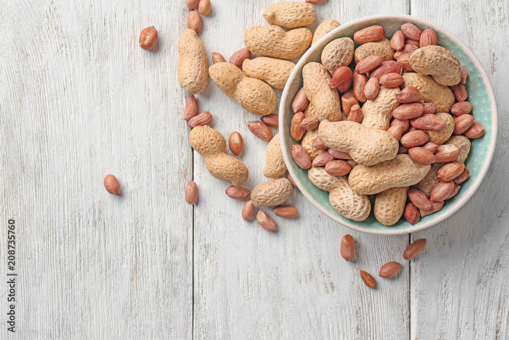 Bowl with peanuts on wooden background