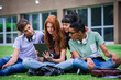 © PhotoAlto - College students sitting on lawn looking at digital tablet together