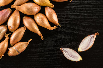 Wall Mural - Long golden shallots one cut in two halves flatlay isolated on black wood background.