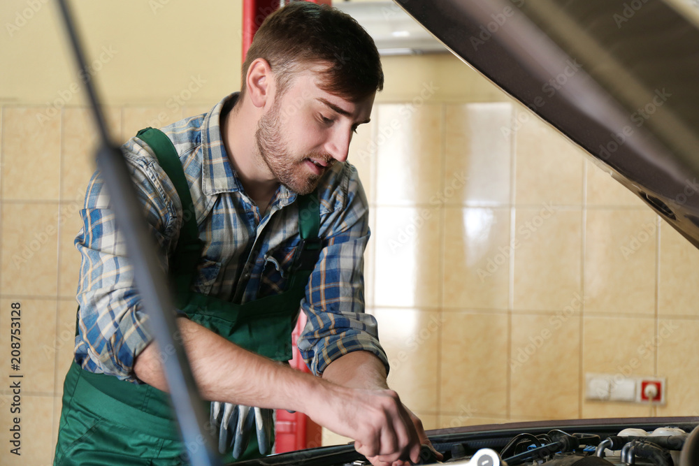 Young auto mechanic repairing car in service center