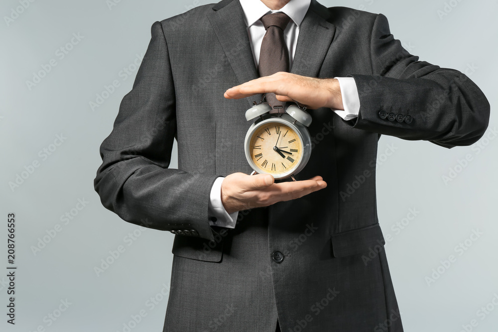 Man holding clock on grey background. Time management concept
