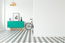 Empty Wall And Turquoise Cabinet With Decorations Standing Next To A Bike In A Hallway Interior With Checkered Floor. Place For Your Poster Or Furniture