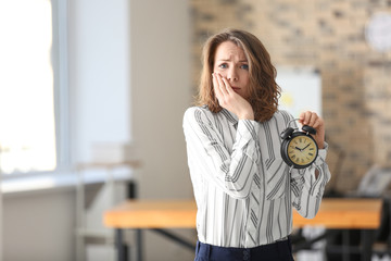 Mature woman with alarm clock in office. Time management concept