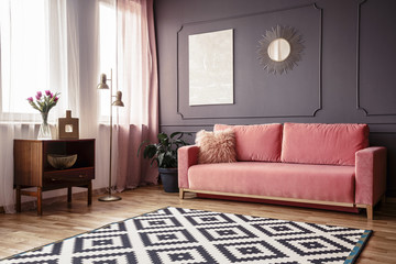 side angle of a living room interior with a powder pink sofa, patterned rug, wooden cabinet and wall