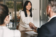 canvas print picture - Business, career and placement concept - image from back of two employers sitting in office and shaking hand of young asian woman, after successful negotiations or interview