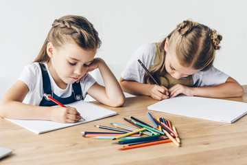 Wall Mural - concentrated little schoolgirls drawing with colorful pencils in albums together isolated on white