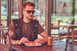© Fxquadro - Portrait of a handsome stylish hipster guy sits at a table, ordered a hamburger and soda, dines at the roadside cafe.