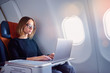 © Loginova - Traveling and technology. Flying at first class. Pretty young businees woman working on laptop computer while sitting in airplane.