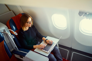 Traveling and technology. Flying at first class. Pretty young businees woman working on laptop computer while sitting in airplane.