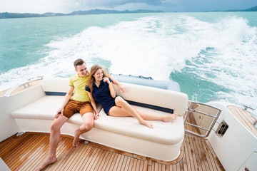 Wall Mural - Romantic vacation and luxury travel. Young loving couple sitting on the sofa on the modern yacht deck. Sailing the sea.