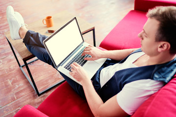 Copy space on the screen. Working at home. Young man using laptop computer while sitting on sofa.