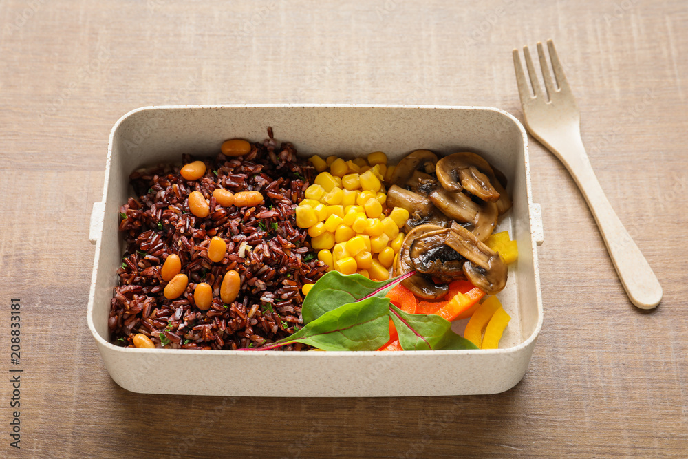 Lunch box with tasty red rice and vegetables on table