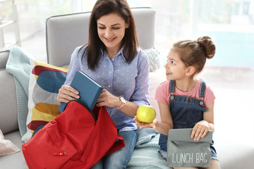 Wall Mural - Young woman helping her little child get ready for school at home