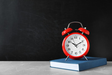 Poster - Alarm clock with book on table against color background. Time concept