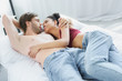 © LIGHTFIELD STUDIOS - multiethnic young couple in love looking at each other while lying in bed together in morning