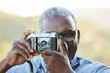 © trinettereed/Stocksy - Close up portrait of African American Senior man taking a photo with a vintage film camera outdoors