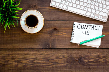 Poster - Template for contacts, background for contact information. Lettering Contact us in notebook on office work desk with computer on dark wooden background top view space for text