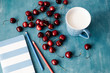 © Laika One/Stocksy - Cherries, sketchbook and a mug of milk on a blue background
