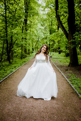  An magnificent bride in a white dress walks along the path in the park