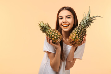 Attractive young woman with two pineapples on color background