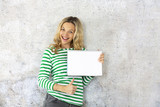 Fototapeta Nowy Jork - young pretty woman with striped pullover holding blank, checkered paper block in the camera.