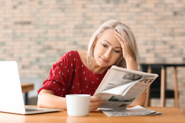 Mature woman reading newspaper in cafe