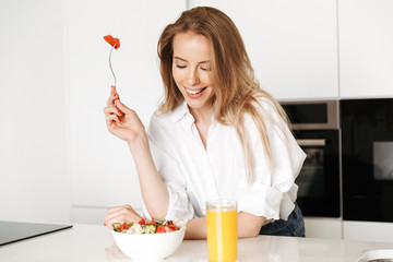 Happy young woman eating salad from a bowl