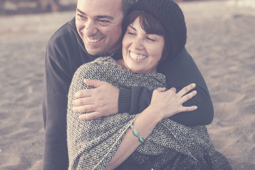 vintage retro look filter colors for nice caucasian middle age couple hugging and having fun together with smiles and laugh. happy leisure activity on the beach in background. romantic lifestyle