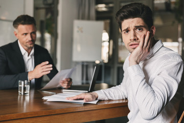 Poster - Business, career and placement concept - stressed nervous man worrying during job interview in office, while negotiating with caucasian businessman or director