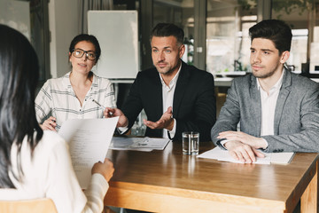 Poster - Business, career and placement concept - three executive directors or head managers sitting at table in office, and interviewing woman with documents or resume in hands