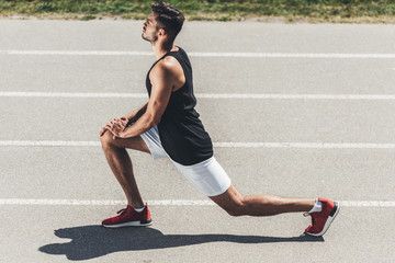 Wall Mural - side view of male jogger stretching on running track at sport playground