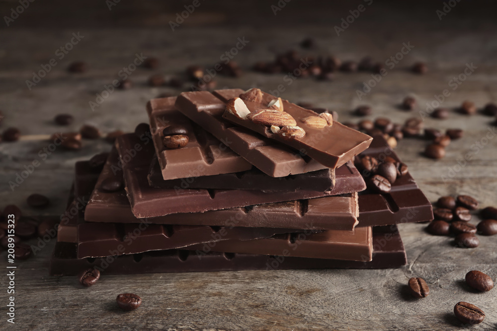 Chocolate bars with almonds and coffee beans on wooden background