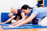 Senior woman and man doing floor gymnastics with physiotherapist