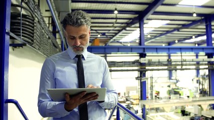 An industrial man engineer standing in a factory, using tablet.
