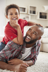 Wall Mural - Son Climbs On Fathers Back As They Play Game In Lounge Together