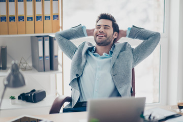 Portrait of glad cheerful man sitting at his desk in workplace, holding two hands behind the head with close eyes imagine holidays vacation weekend