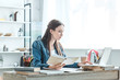 © LIGHTFIELD STUDIOS - focused teenage girl holding book and using laptop while studying at home