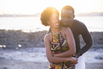 beautiful couple of black race african models in traditional dress have fun and love together at the beach in summer during the sunset. nice backlight from sun, outdoor relationship concept