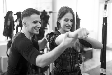 Concentrated woman working out ems training with his coach. Personal trainer helps the girl during the exercise