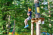 brave young boy in helmet climbs on tree tops in amusement rope park on summer holidays, children camp