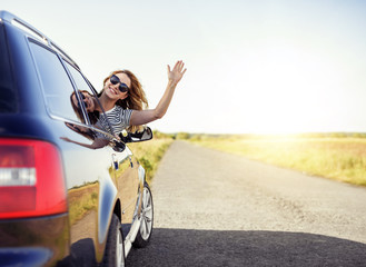 Wall Mural - Attractive smiling woman waving her hand from the car window on a summer day.