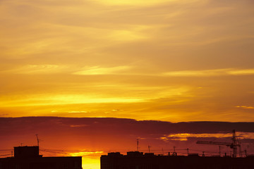 Wall Mural - Beautiful cloudy dramatic morning sky above silhouette of city buildings. Picturesque dawn in city. Background of varicolored clouds. Unimaginable fantasy sunrise in heaven. Silhouette of tower crane.