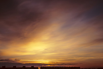 Wall Mural - Beautiful cloudy dramatic morning sky above silhouette of city buildings. Picturesque dawn in city. Aircraft trail on vivid clouds. Background from unimaginable fantasy sunrise in heaven.