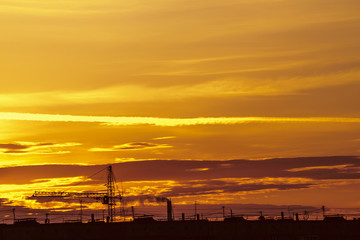 Wall Mural - Beautiful cloudy dramatic morning sky above silhouette of city buildings. Picturesque dawn in city. Aircraft trail on vivid clouds. Unimaginable fantasy sunrise in heaven. Silhouette of tower crane.